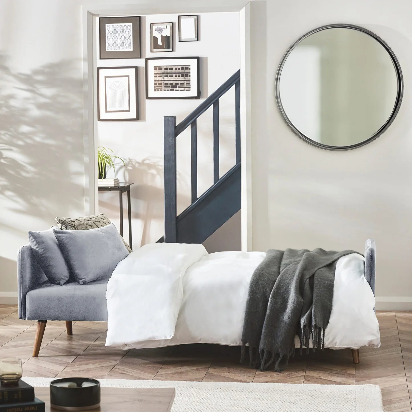 Modern bedroom with a sofa bed and round mirror.