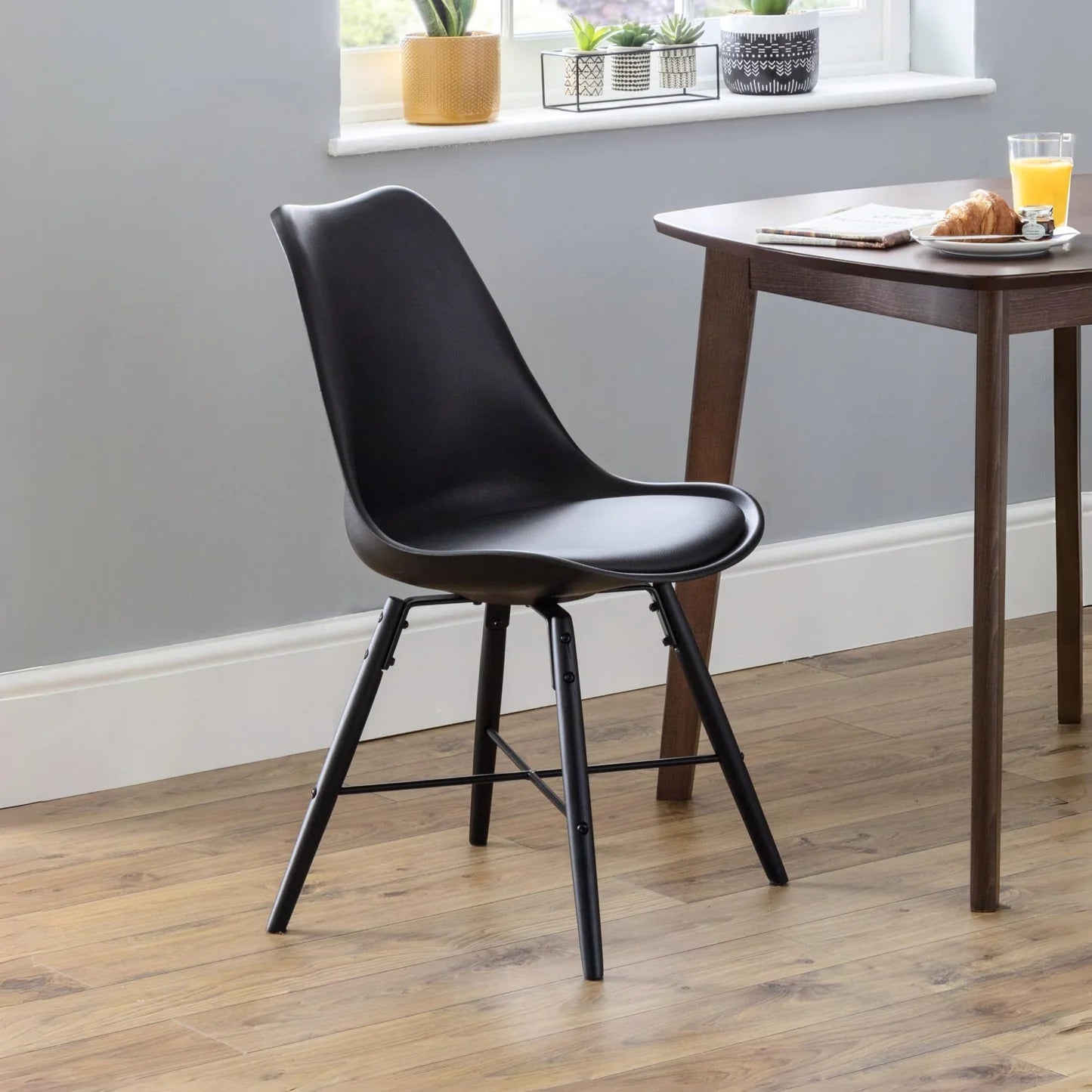 Black chair in a room with a wooden table and window sill with plants.