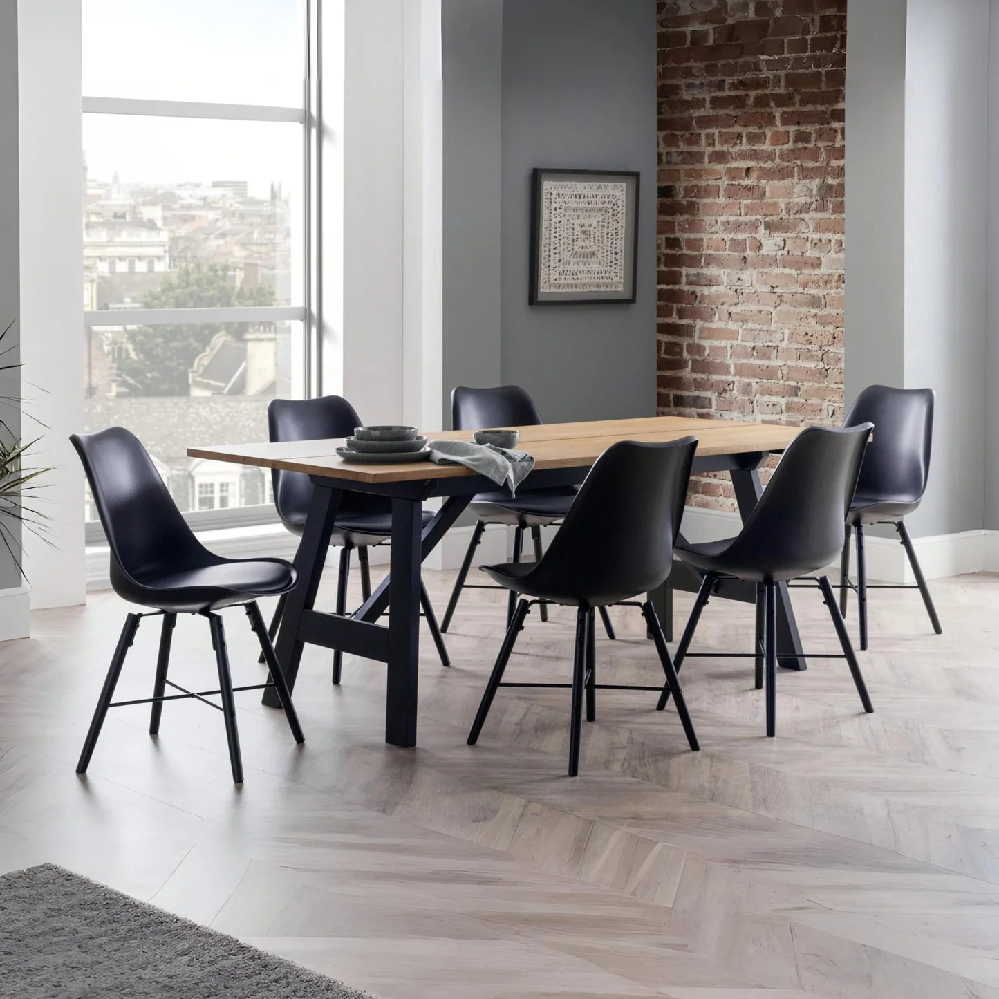Dining room with a wooden table and black chairs in front of a brick wall.
