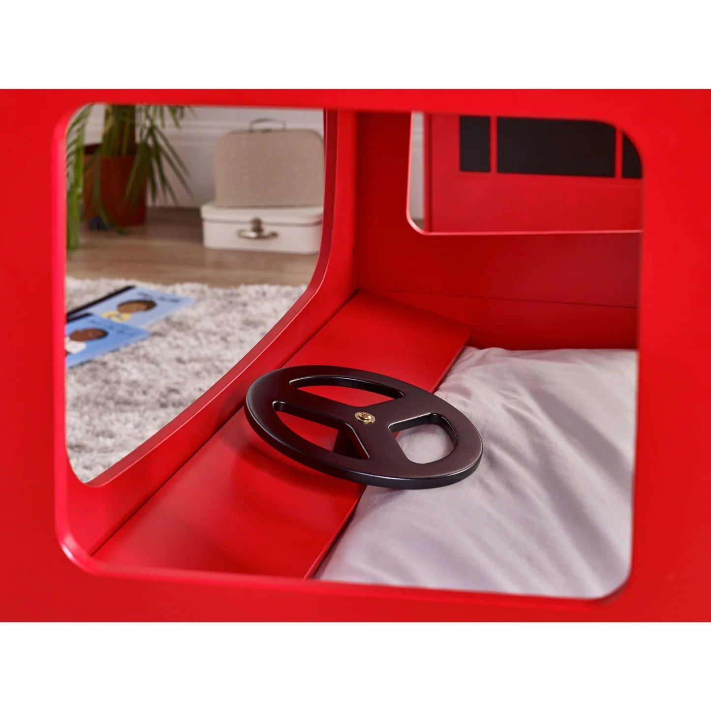 Red playpen with a black wheel inside, showing a room with toys and furniture in the reflection.