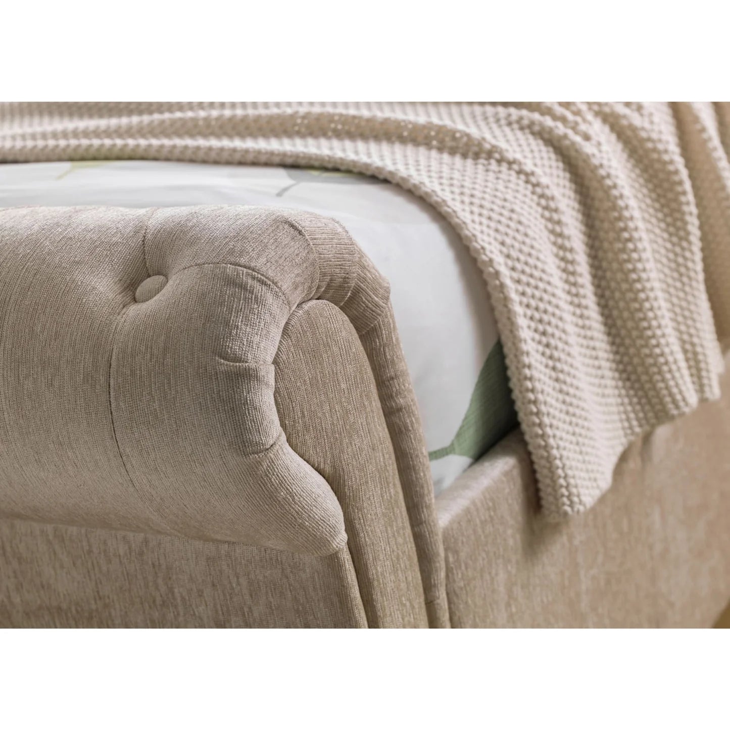 Close-up of a beige upholstered headboard with a textured blanket draped over it.