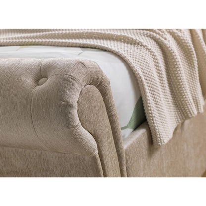 Close-up of a beige upholstered headboard with a textured blanket draped over it.